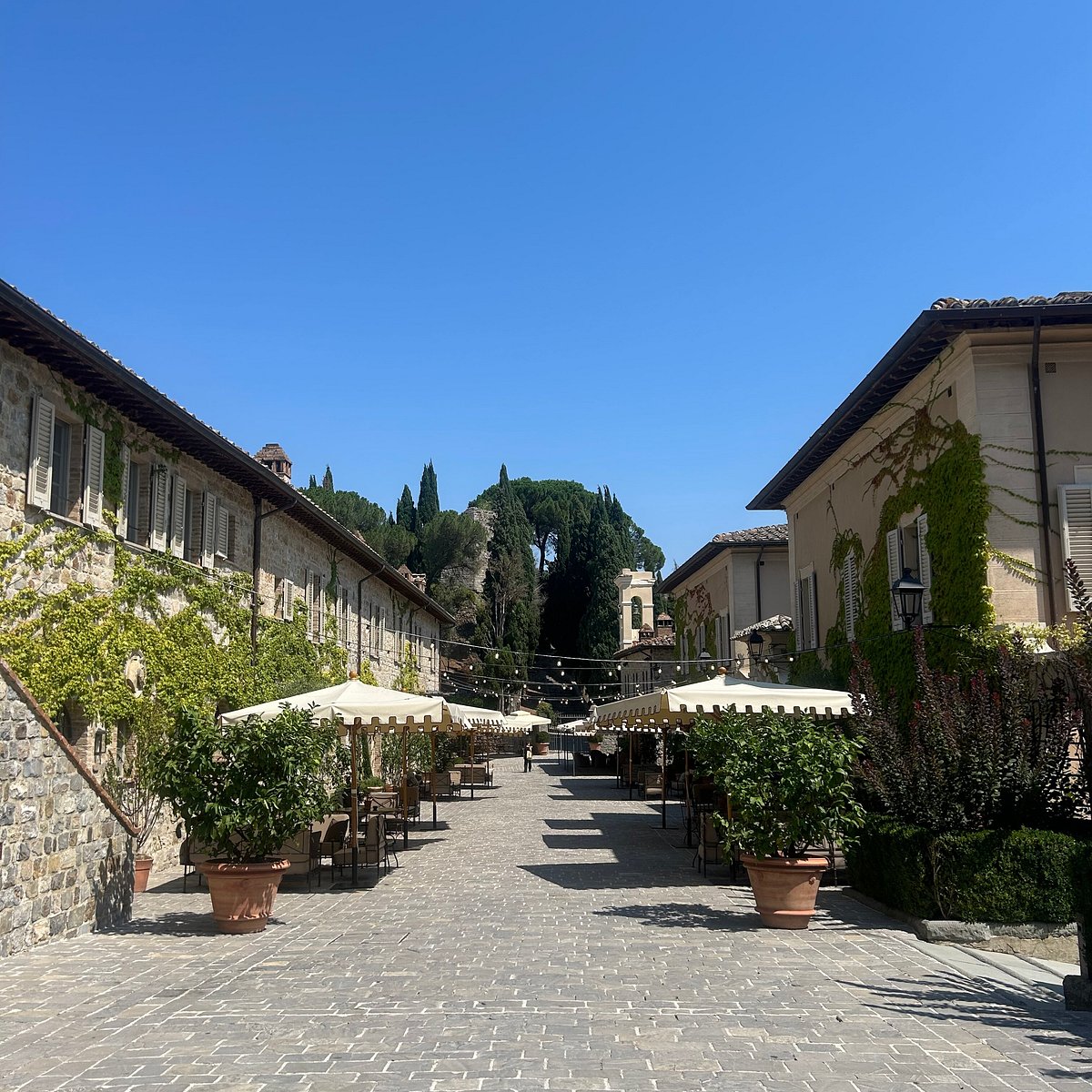 The piazzetta at Castiglion del Bosco — cobbled stone, canopied tables, and cypress-covered hills rising behind the borgo.